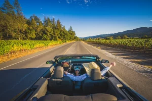 Ein Paar fährt in einem Cabrio den Silverado Trail entlang, umgeben von Weinbergen und blauem Himmel im Napa Valley.