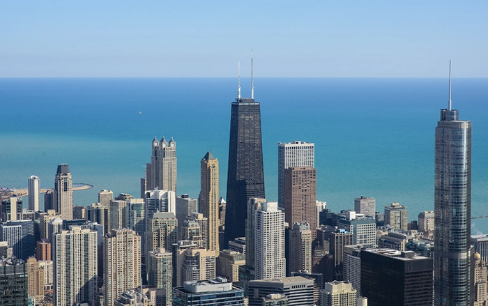 Blick vom Skydeck im Willis Tower auf die Hochhäuser Chicagos mit dem markanten John Hancock Center und dem tiefblauen Lake Michigan im Hintergrund.