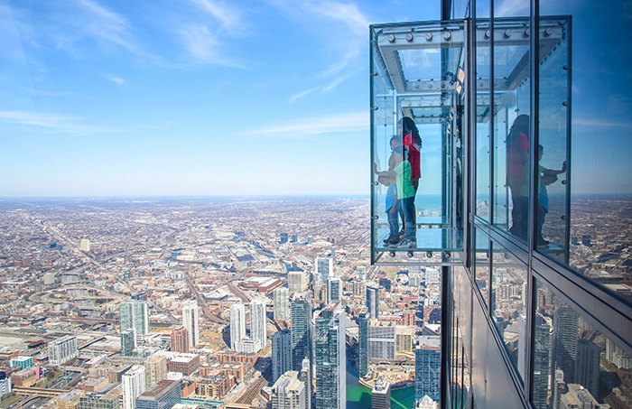 Personen stehen auf der gläsernen Aussichtsplattform des Skydeck im Willis Tower und blicken über die Skyline von Chicago.