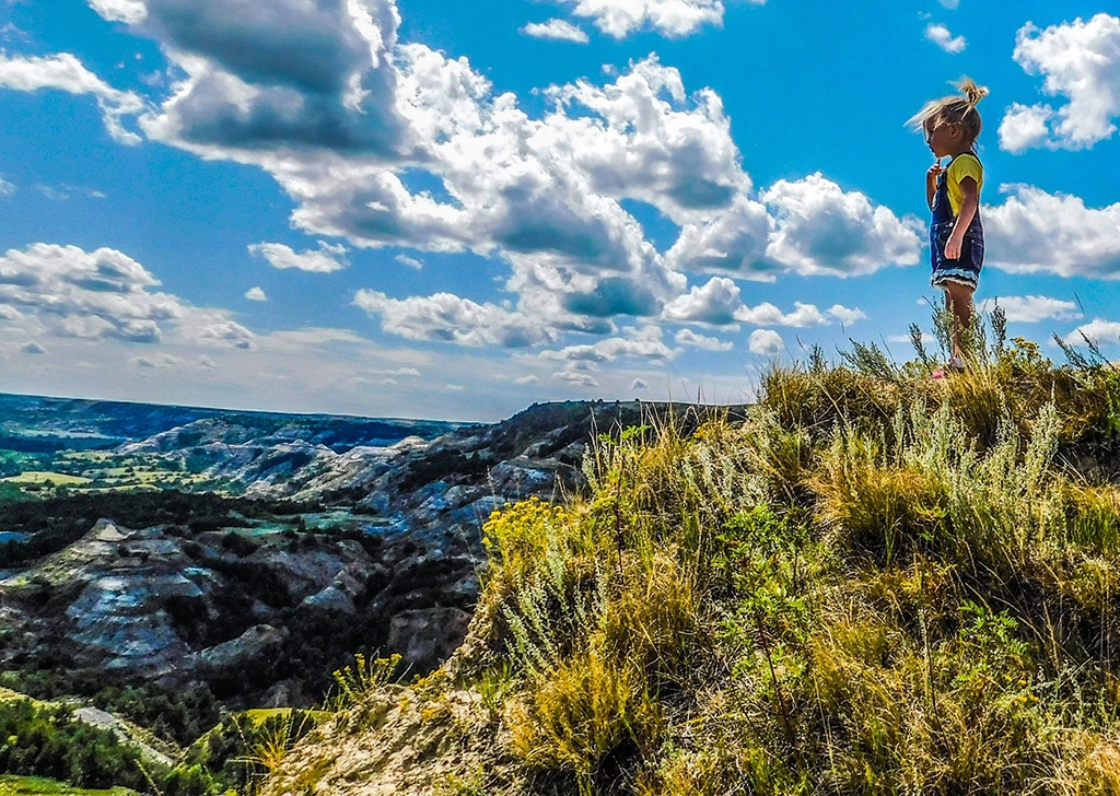 Ein kleines Mädchen steht auf einem Hügel und schaut über die zerklüfteten Badlands des Theodore Roosevelt Nationalparks.