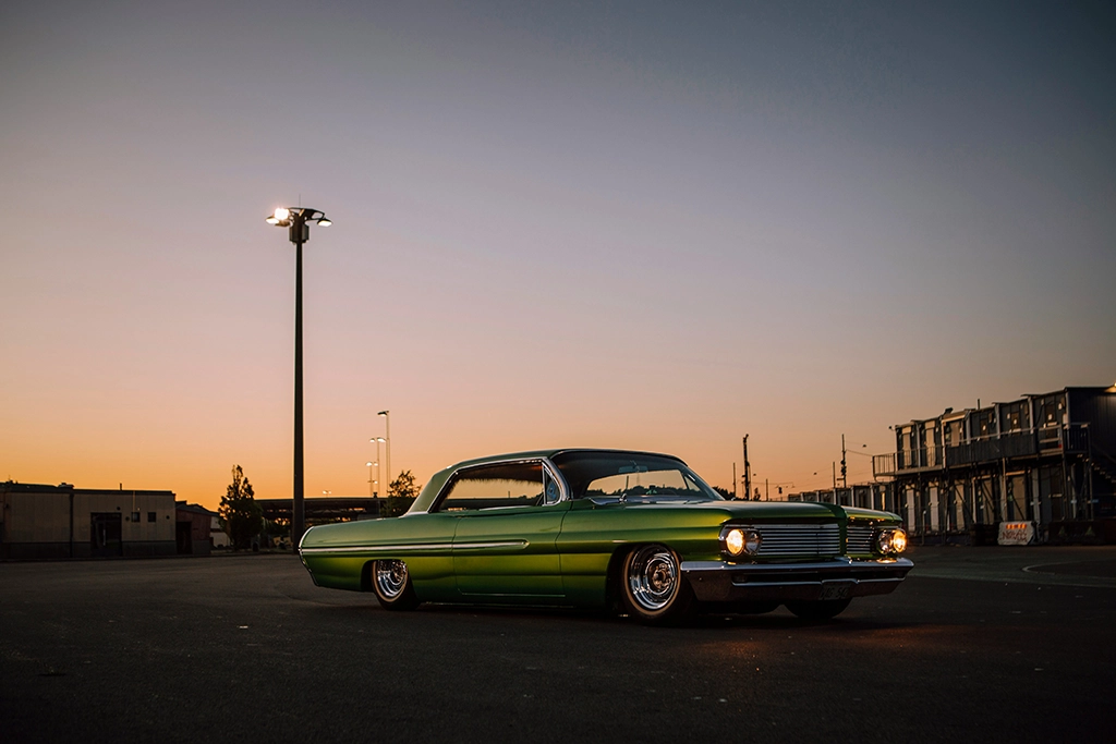 Grüner Lowrider im Sonnenuntergang auf einem leeren Parkplatz, im Hintergrund Industriebauten.