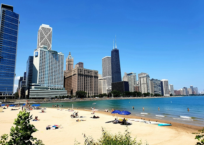 Sonnenhungrige Menschen am Oak Street Beach in Chicago mit Blick auf die Skyline und den Hancock Tower am Ufer des Lake Michigan.