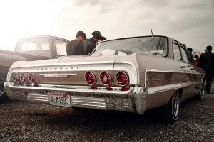Klassischer Chevrolet Impala aus den 1960er-Jahren mit verchromtem Heck und Washington-Kennzeichen, umgeben von Autoliebhabern.