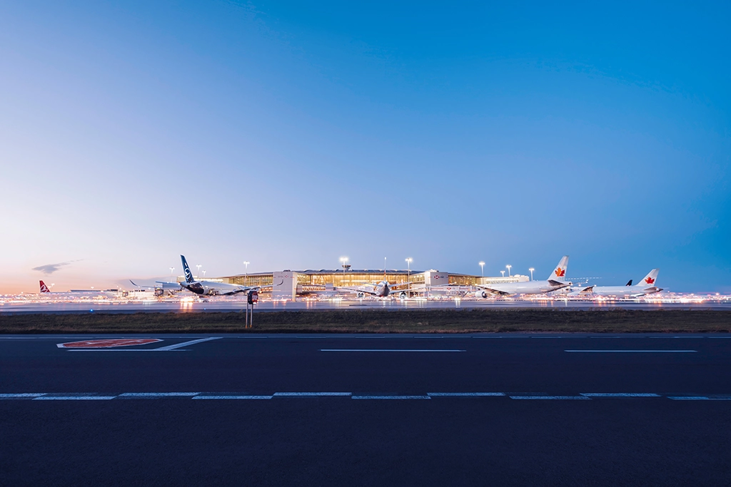 Flugzeuge verschiedener Airlines stehen am beleuchteten Flugfeld des Toronto Pearson Flughafens in der Dämmerung.