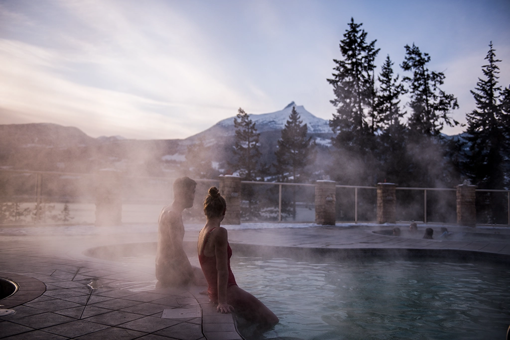 Zwei Personen entspannen im Halcyon Hot Springs Resort bei Nakusp mit Blick auf die verschneiten Berge.