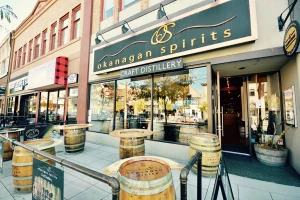 Außenansicht der Okanagan Spirits Craft Distillery in Downtown Kelowna mit Fass-Tischen vor dem Eingang