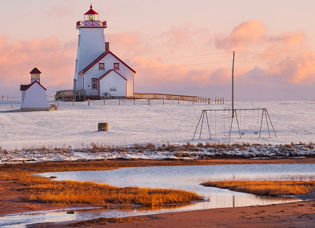 Verschneiter Leuchtturm in Wood Islands auf Prince Edward Island, im Abendlicht mit Schaukeln im Vordergrund.