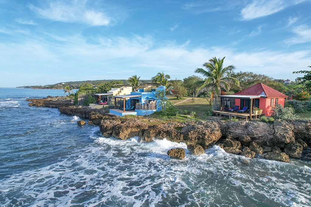 Farbenfrohe Bungalows stehen direkt auf den Felsen an Jamaikas Südküste, umgeben von Palmen und Meeresrauschen.