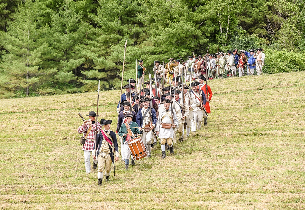 Historische Darsteller in Uniformen der Amerikanischen Revolution marschieren über ein Feld
