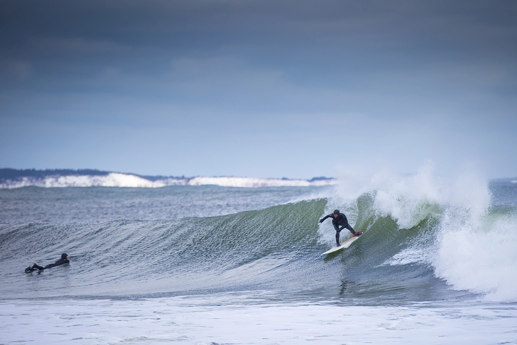 Zwei Surfer in Neoprenanzügen reiten winterliche Wellen an der Küste von Lawrencetown, Nova Scotia