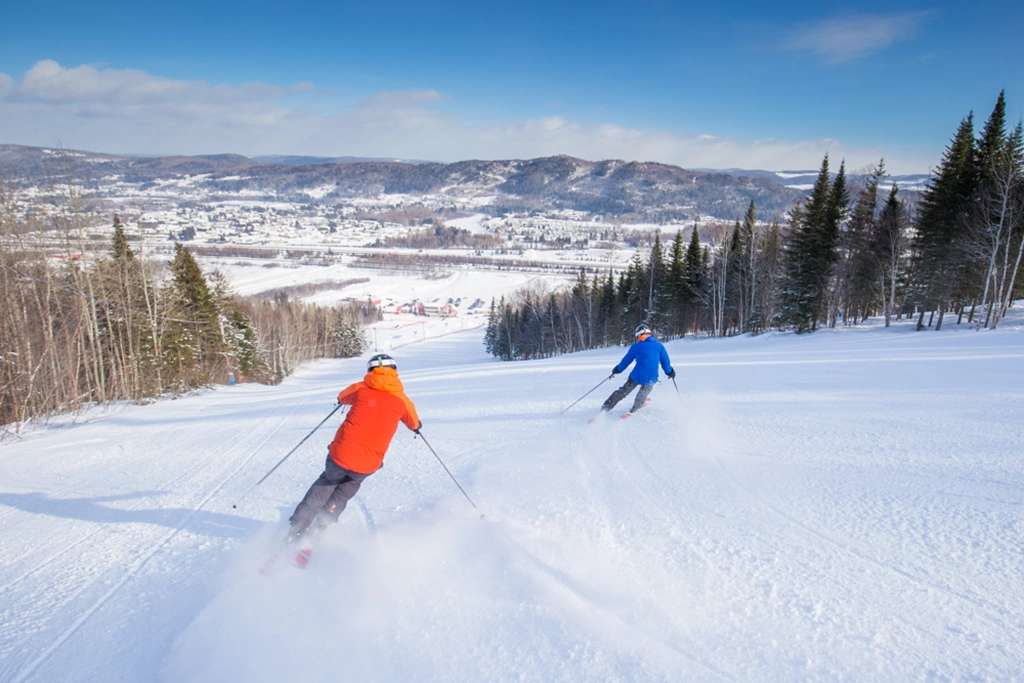 Zwei Skifahrer auf einer verschneiten Piste mit Blick auf das Tal bei Edmundston im Mount Farlagne Outdoor Centre, New Brunswick.