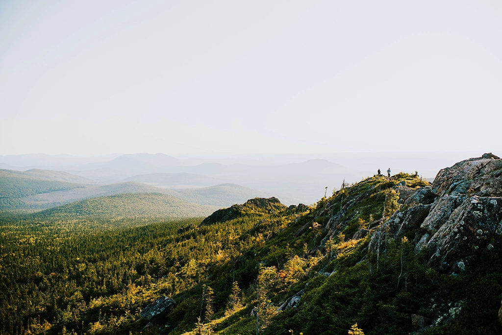 Zwei Wanderer auf einem Bergrücken mit weitem Blick über das bewaldete Hügelland im Mount Carleton Provincial Park in New Brunswick.