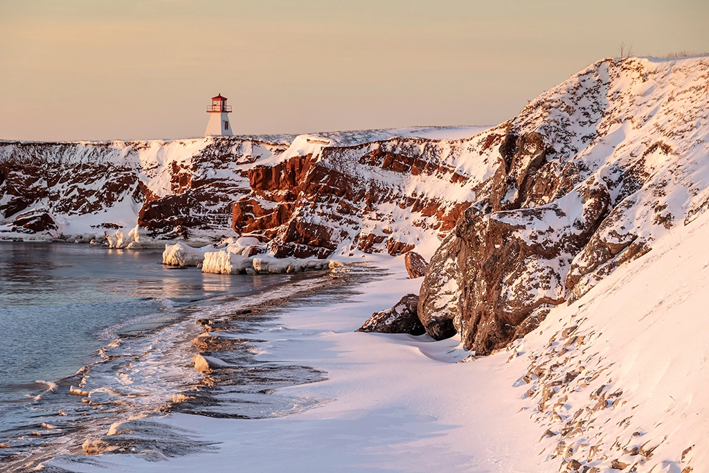 Leuchtturm auf roten Klippen im Schnee auf den Îles de la Madeleine, Québec