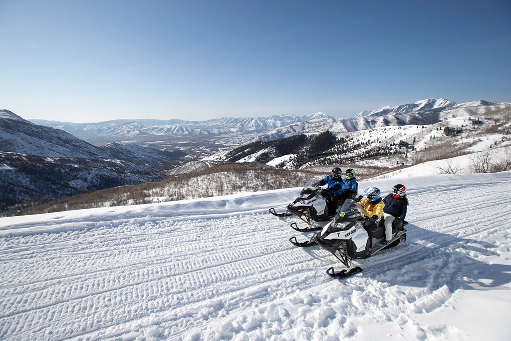 Vier Personen fahren auf Schneemobilen durch die verschneite Berglandschaft des Heber Valley, Utah