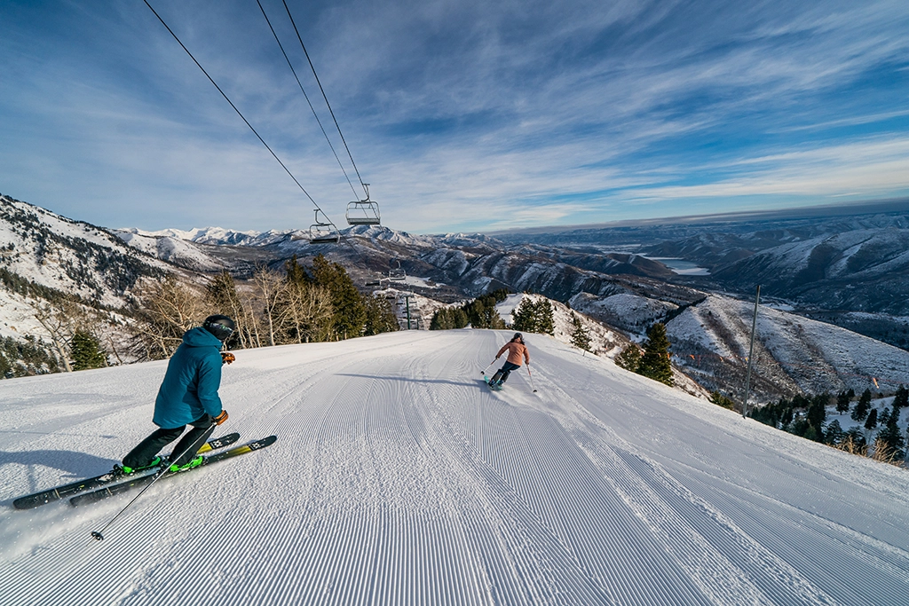 Zwei Skifahrer auf einer frisch präparierten Piste im Sundance Resort, Utah, mit Panoramablick auf die verschneiten Berge.