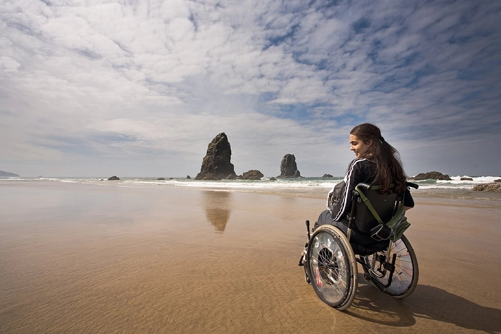 Frau im Rollstuhl am Cannon Beach mit Blick auf Haystack Rock, Oregon Coast