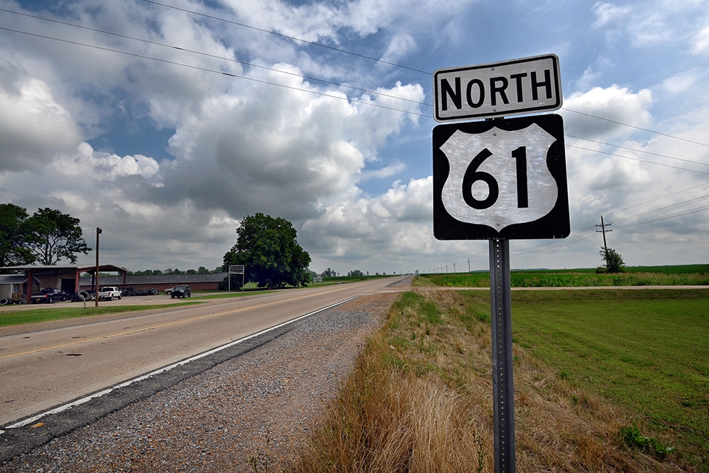 Blick auf den U.S. Highway 61 in Mississippi, umgeben von Feldern und unter einer dramatischen Wolkendecke.