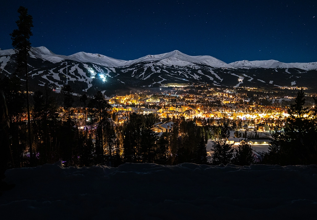 Nächtliche Panoramaaufnahme von Breckenridge mit beleuchteten Häusern und Skipisten.