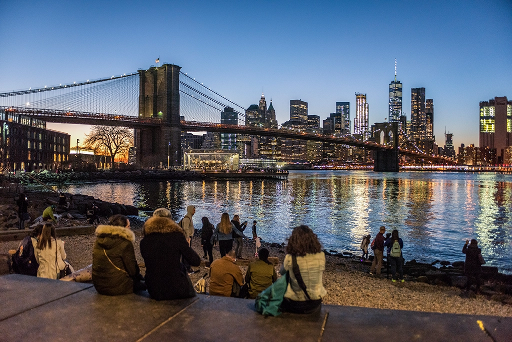 Menschen im Brooklyn Bridge Park mit Blick auf Brooklyn Bridge und Skyline von Manhattan bei Abendlicht
