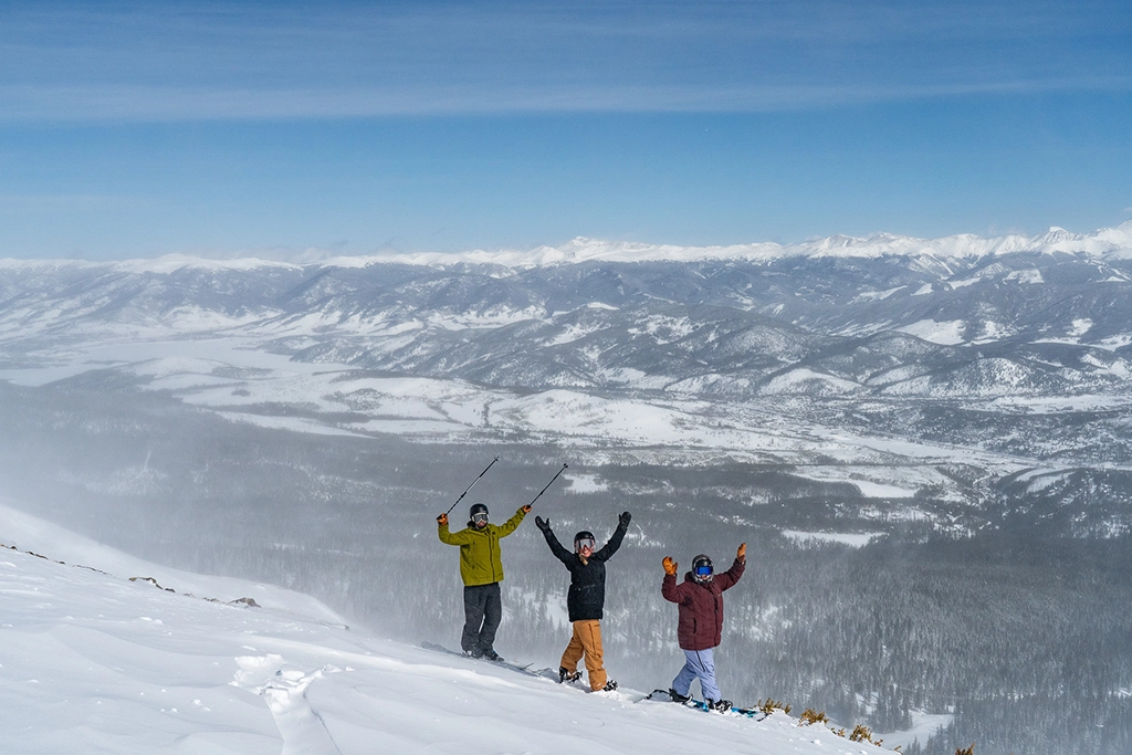 Drei Skifahrer stehen auf einem verschneiten Grat mit Blick über die Berglandschaft am Copper Mountain.