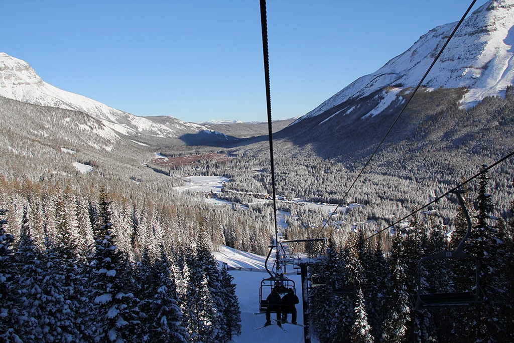 Sesselliftfahrt im Skigebiet Castle Mountain mit Blick auf verschneite Wälder und das Tal in den kanadischen Rocky Mountains.