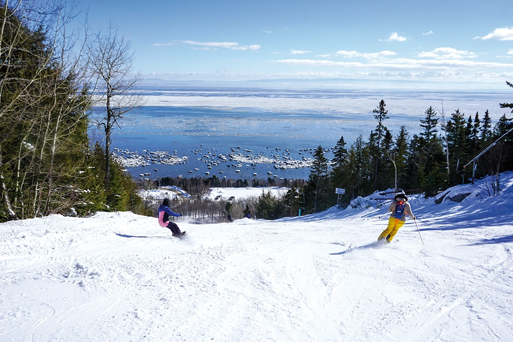 Skifahrer auf einer Abfahrt im Skigebiet Le Massif de Charlevoix mit Blick auf den gefrorenen Sankt-Lorenz-Strom