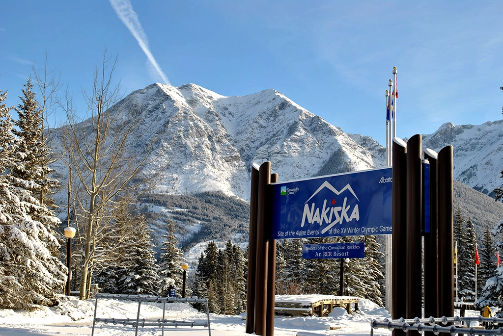 Eingangsschild des Skigebiets Nakiska in Kananaskis Country vor verschneiten Bergen in Alberta, Kanada.