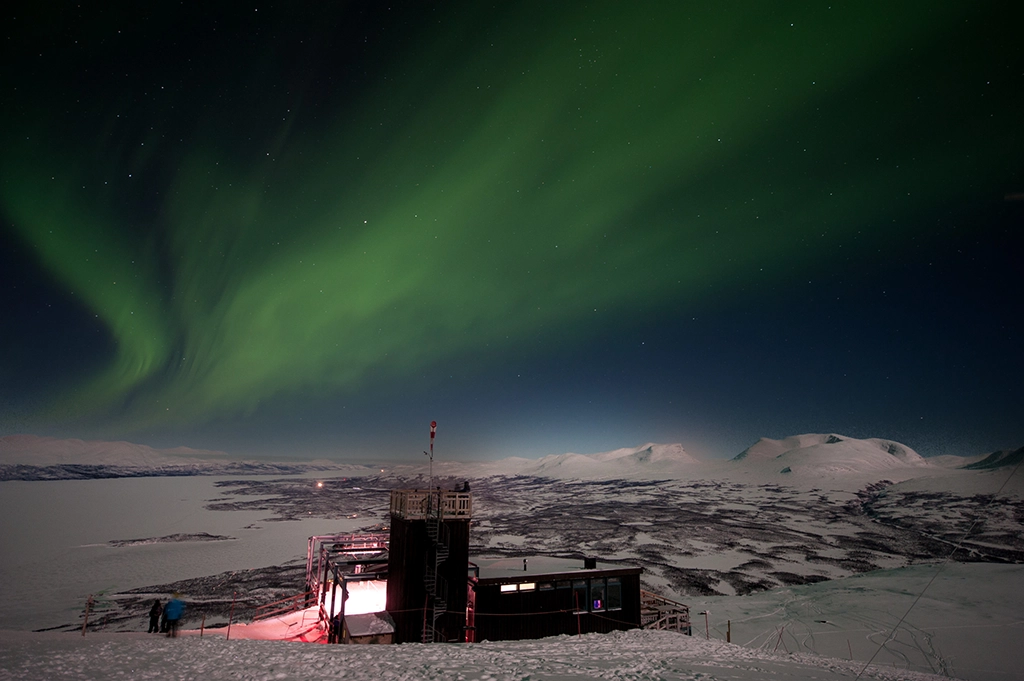 Nordlichter über einer verschneiten Berglandschaft in Abisko mit Polarlicht in kräftigem Grün.