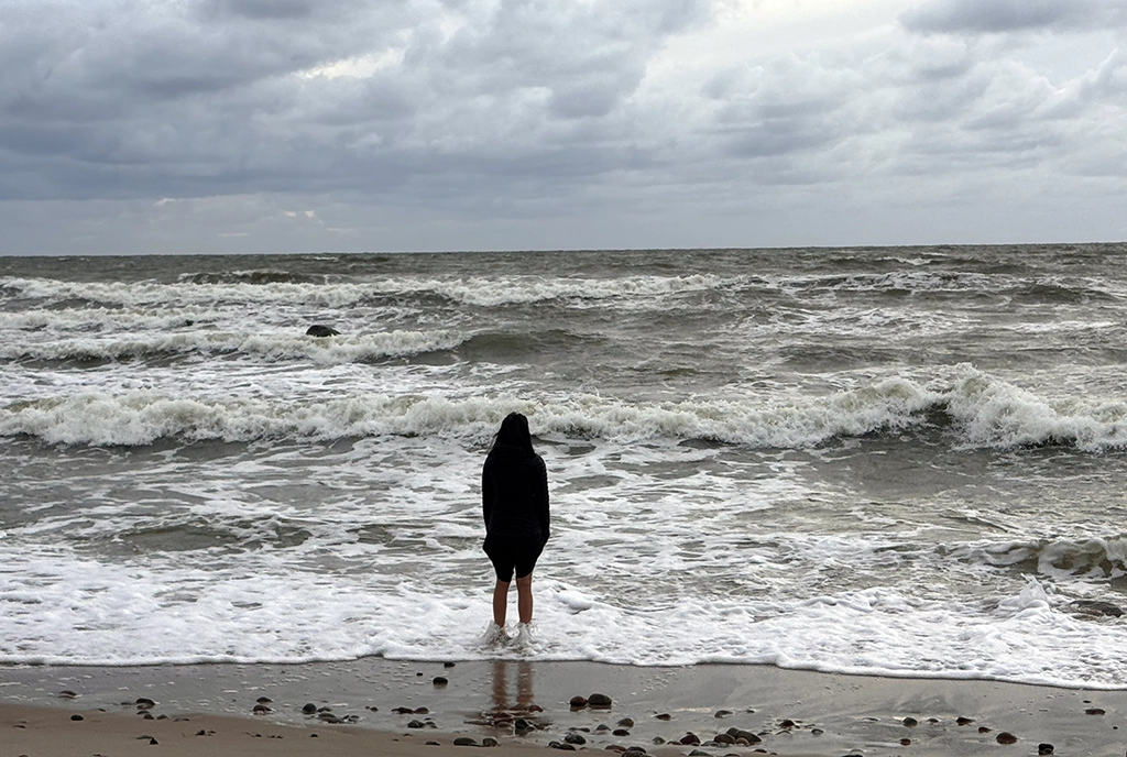 Person steht an der stürmischen Ostseeküste in Litauen und blickt auf die Brandung