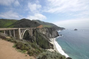 Blick auf den Highway 1 in Big Sur mit steilen Klippen und türkisblauem Meer im Hintergrund