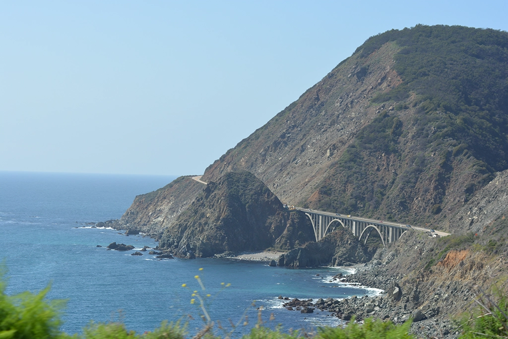 Auto fährt entlang des Highway 1 in Big Sur mit grünen Berghängen und Küstenlandschaft