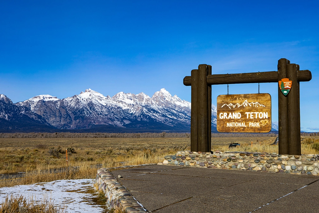 Holzschild mit Aufschrift Grand Teton National Park vor verschneiter Gebirgskette