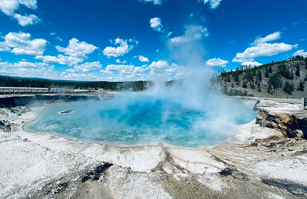 Dampfen über einer türkisfarbenen heißen Quelle im Yellowstone Nationalpark, umgeben von Wald und Holzstegen