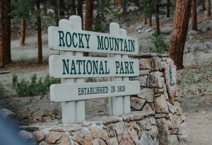 Holzschild mit Aufschrift „Rocky Mountain National Park – Established in 1915“ in bewaldeter Umgebung