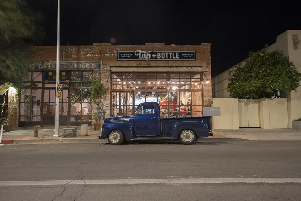 Historisches Backsteingebäude mit Glasfassade, davor ein blauer Oldtimer-Pick-up. Nachtaufnahme in Downtown Tucson.