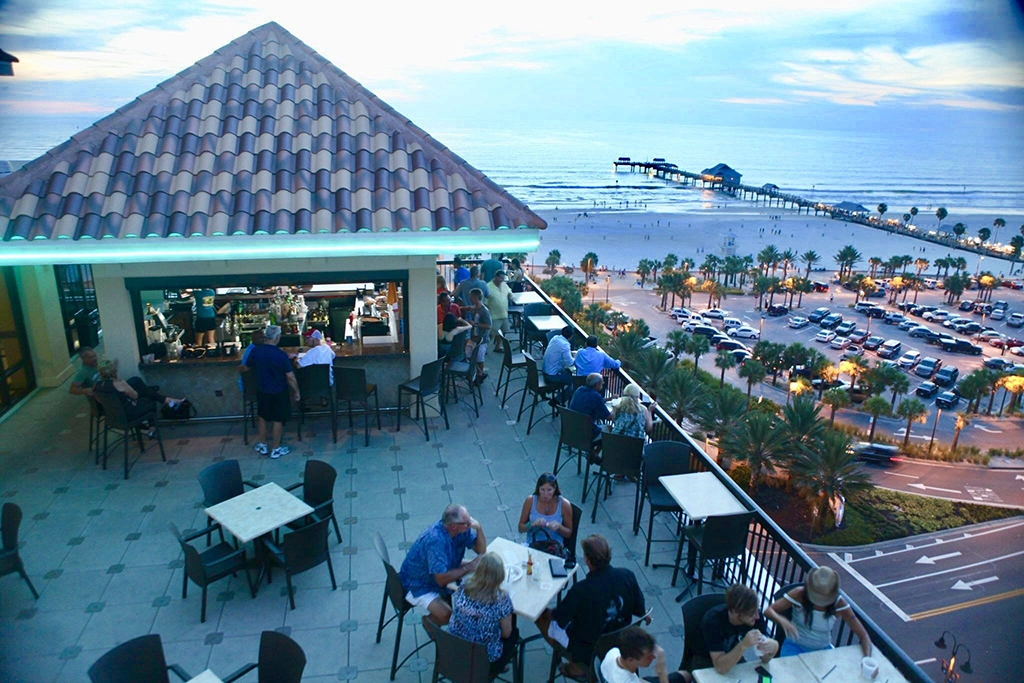 Gäste genießen den Ausblick von Jimmy’s Crow’s Nest auf den Strand und Pier 60 bei Sonnenuntergang.