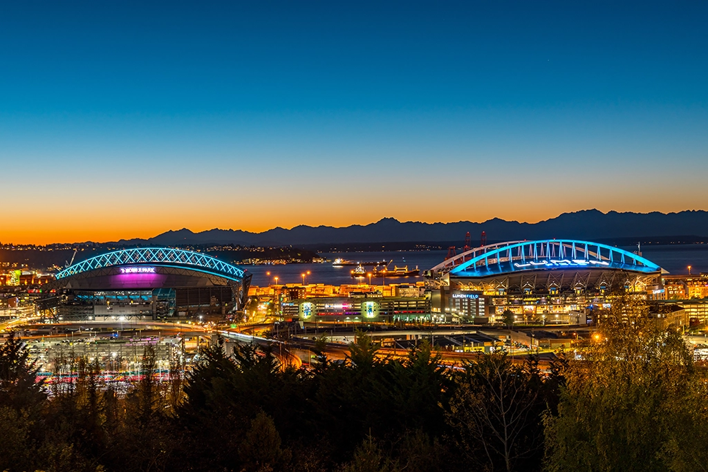 Lumen Field in Seattle bei Nacht mit beleuchteten Stadionbögen und Skyline.