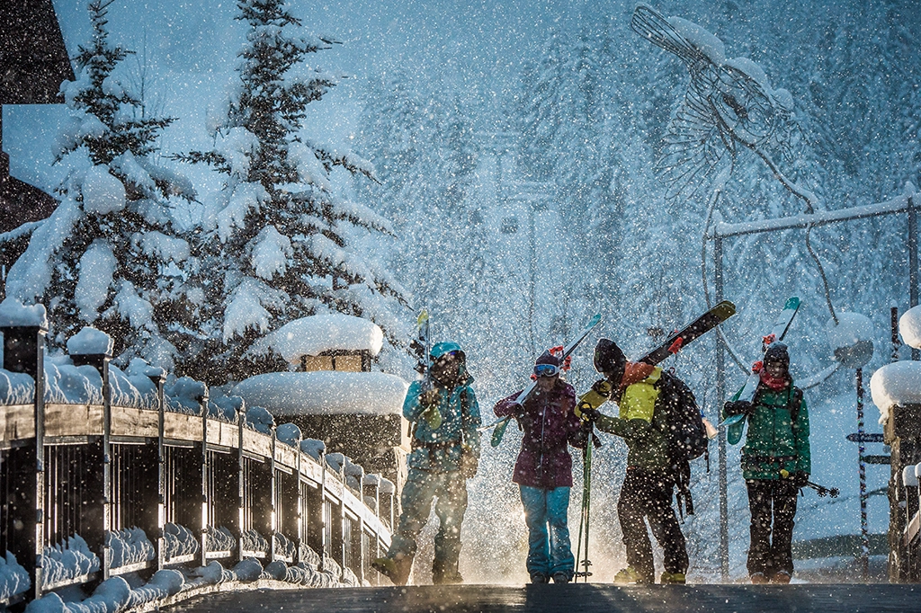 Skifahrer mit Ausrüstung auf verschneiter Brücke in Whistler Village bei Schneefall.