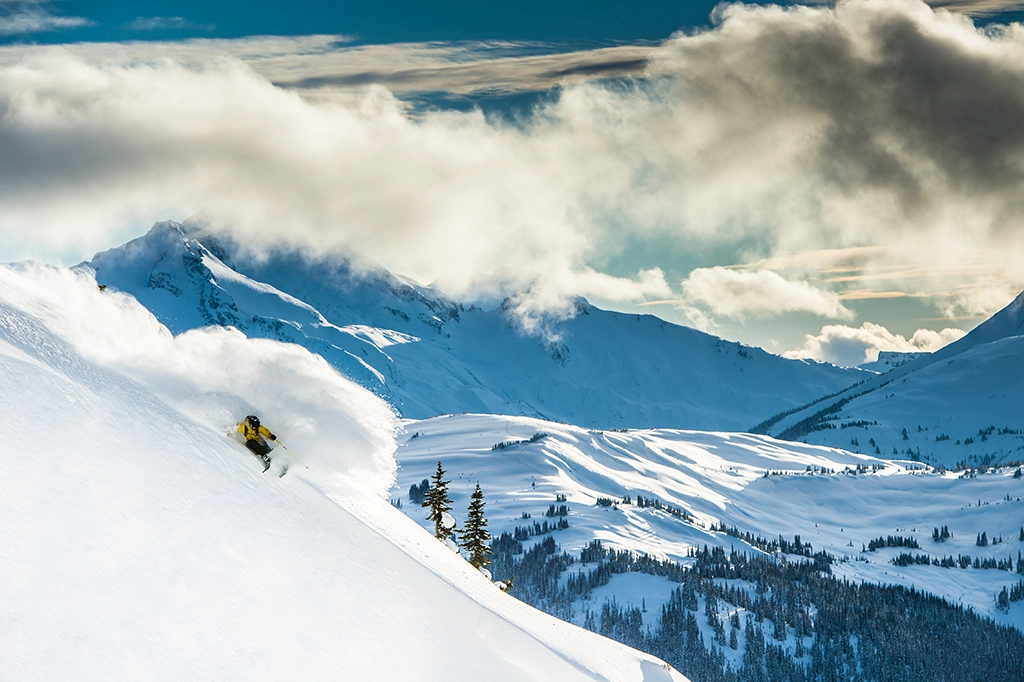 Skifahrer im Tiefschnee am Whistler Blackcomb mit Blick auf verschneite Gipfel der Coast Mountains.
