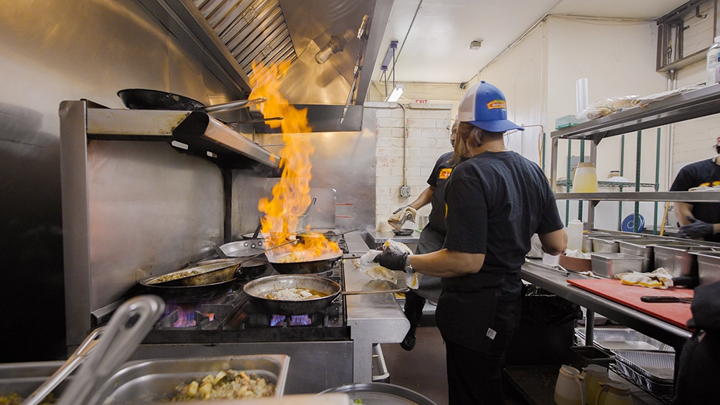 Köchin bereitet Gericht mit offener Flamme in der Küche von Tumerico Tucson zu.