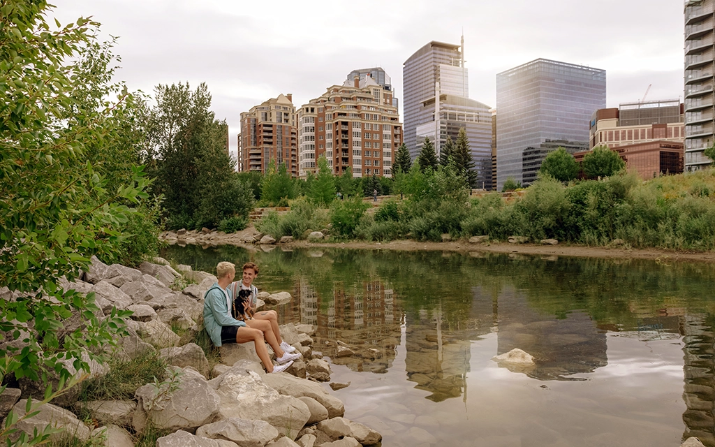 Paar sitzt am Flussufer mit Blick auf die Skyline von Calgary in Alberta.