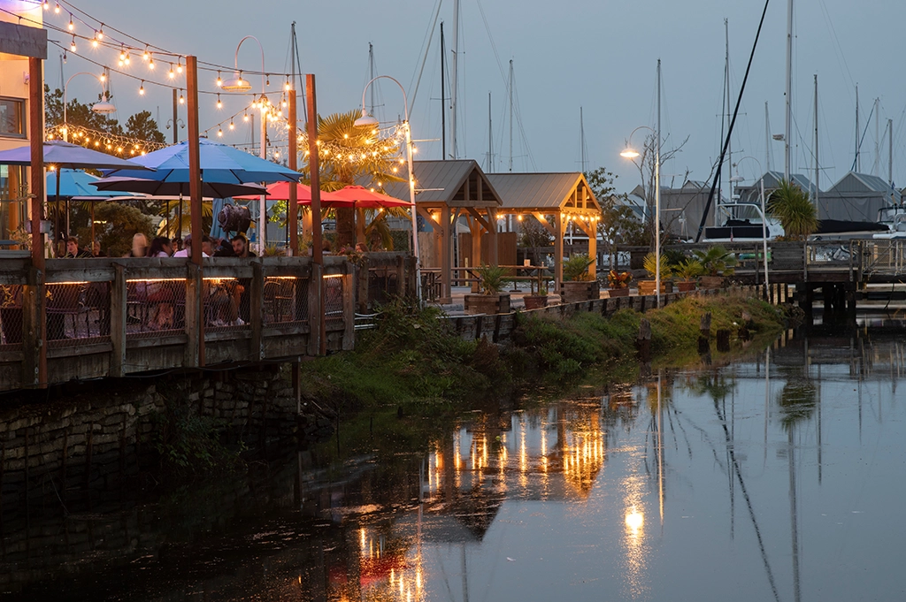 Beleuchtete Uferpromenade in Olympia am Abend mit reflektierenden Lichtern im Wasser.
