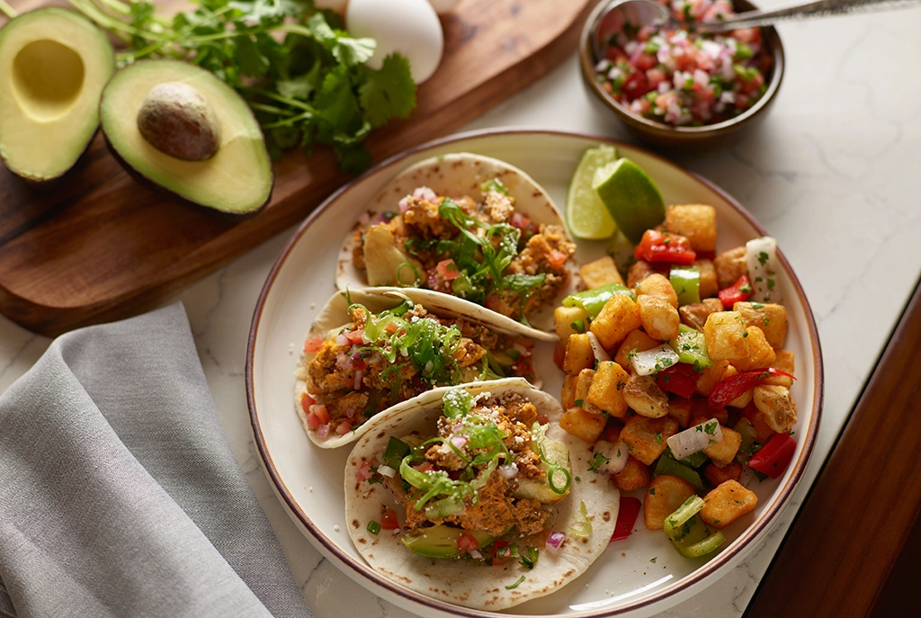 Frühstückstacos mit Avocado, Gemüse, Eiern und Kartoffeln auf einem gedeckten Tisch