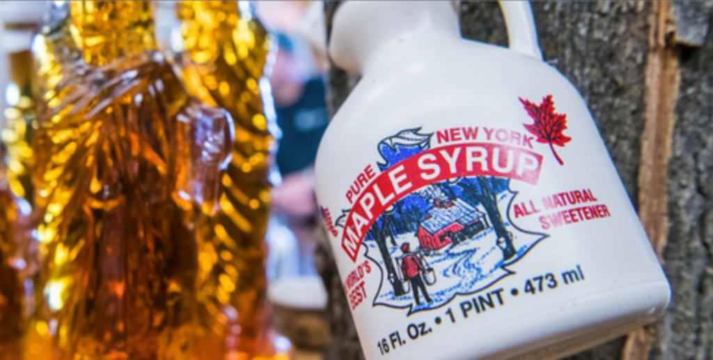 Flasche mit reinem Ahornsirup aus New York vor goldfarbenem Hintergrund.