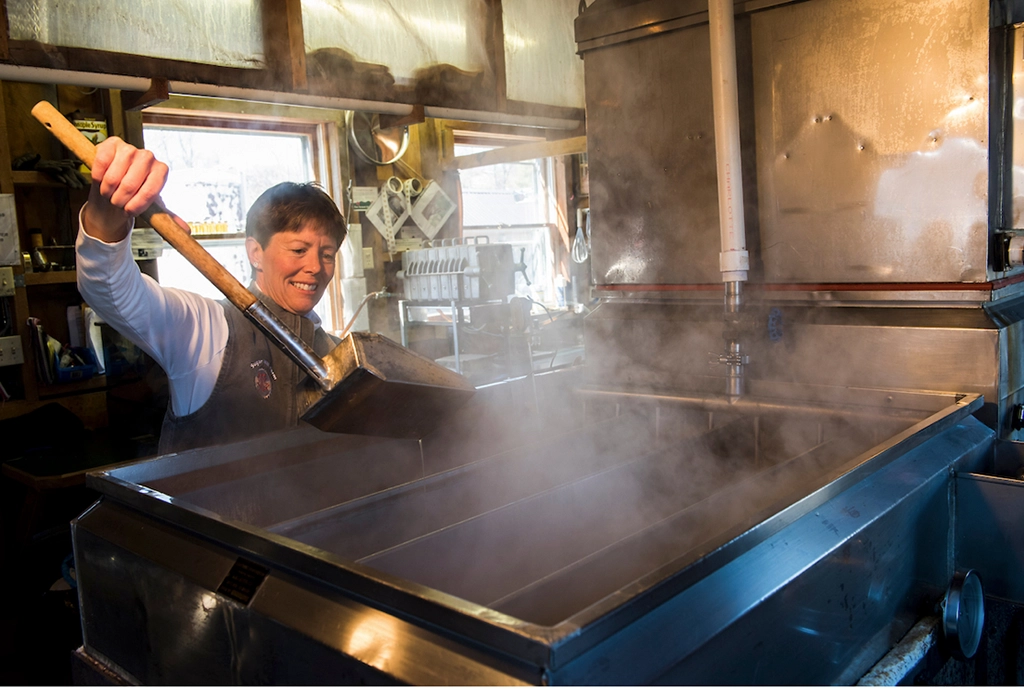 Mitarbeiterin kocht Ahornsirup in großen Edelstahlkesseln in einer Zuckerhütte.