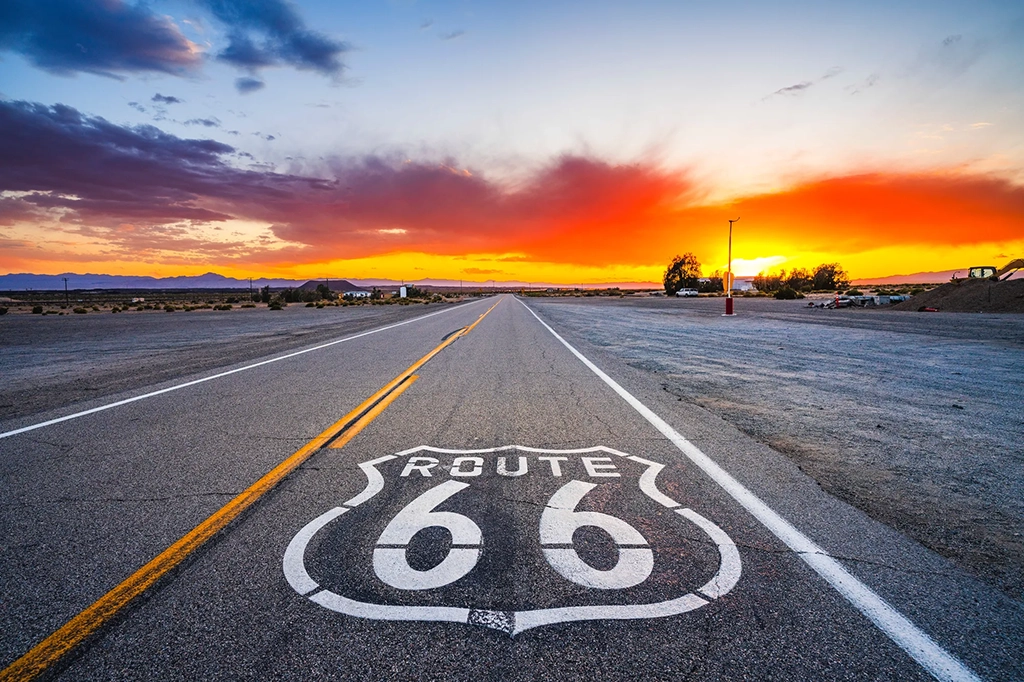 Straßenmarkierung der Route 66 auf einer Wüstenstraße bei Sonnenuntergang.