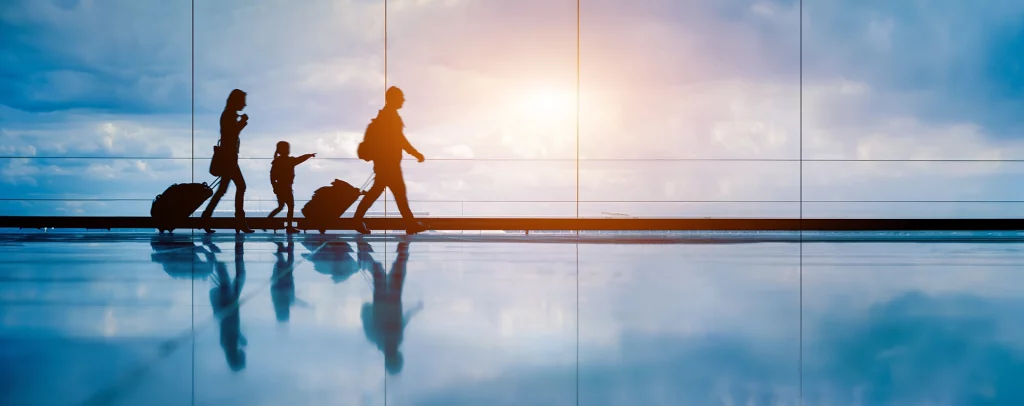Familie mit Rollkoffern in einem Flughafen-Terminal vor großer Glasfront.