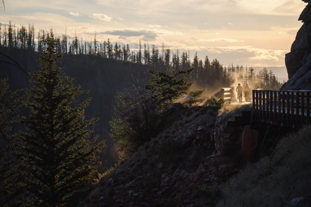Radfahrer auf Holzsteg entlang des Kettle Valley Rail Trail bei Sonnenaufgang in bergiger Landschaft