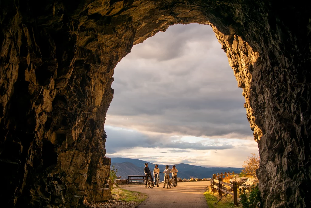 Blick aus Felsentunnel auf Radfahrer und Berglandschaft am Kettle Valley Rail Trail