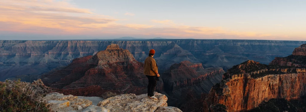Besucher steht bei Sonnenuntergang am North Rim des Grand Canyon mit Blick über die Schlucht.